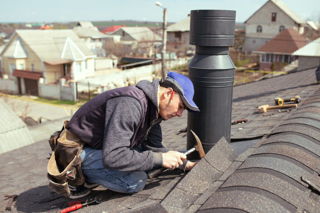 A workman completing roof work, he is using a hammer and wearing a blue cap with a tool bag attached 