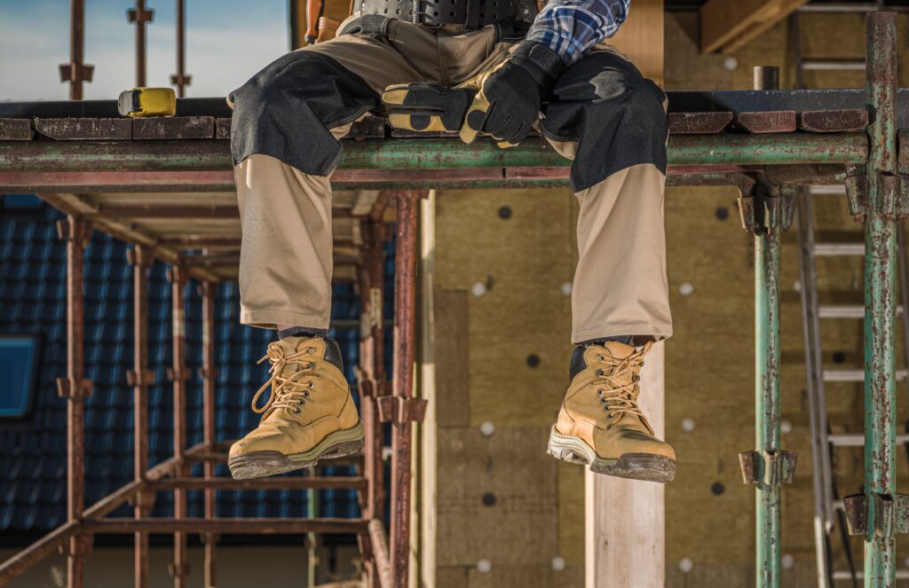 A mans legs dangling off a platform he is wearing work boots